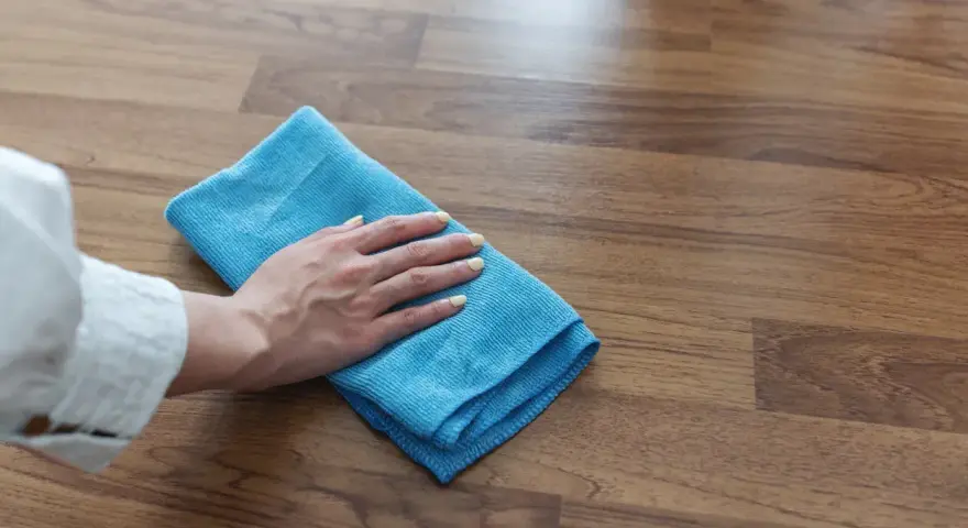 Mano con panno blu pulisce superficie in legno, mostrando come togliere la colla dal legno con delicatezza.