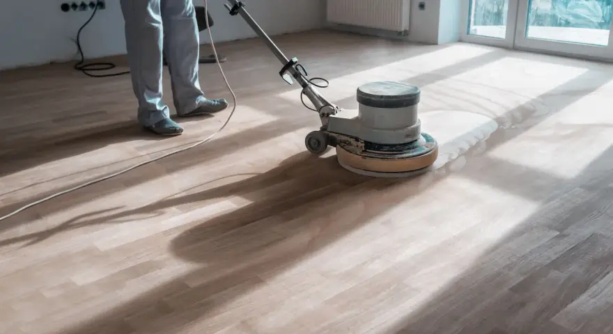 Un professionista usa una levigatrice per decerare il parquet, sollevando una nuvola di polvere.