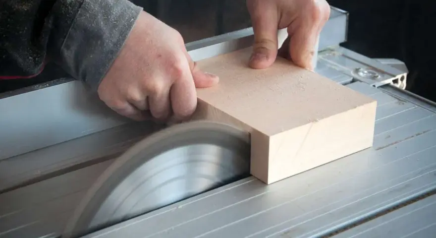 Mani esperte guidano un pezzo di legno su una sega circolare per tagliare legno a mano con precisione.