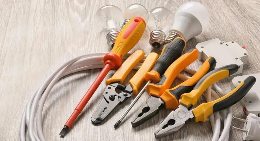 Un set di strumenti per elettricisti: pinze, cacciaviti, lampadine e cavi su un tavolo di legno.