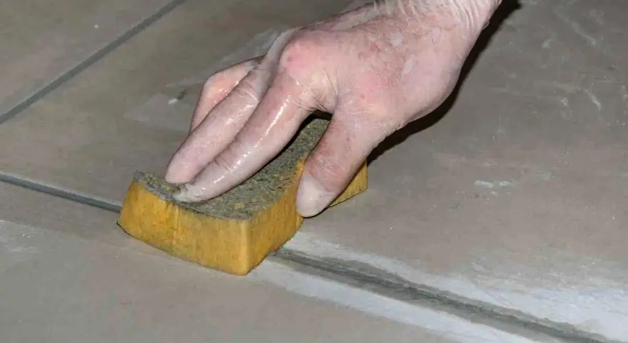Mano con guanto in lattice che rifinisce le fughe dei pavimenti con una spugna umida.
