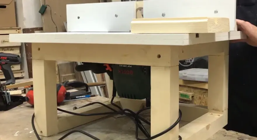 Banco fresa fai da te con fresatrice Bosch montata sotto il piano di lavoro. Un pezzo di legno viene lavorato.