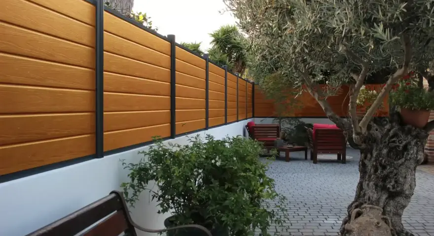 Pannello in legno effetto teak fissato a un muro bianco, con un ulivo secolare e arredi da esterno. Ideale per capire come fissare un pannello di legno al muro.