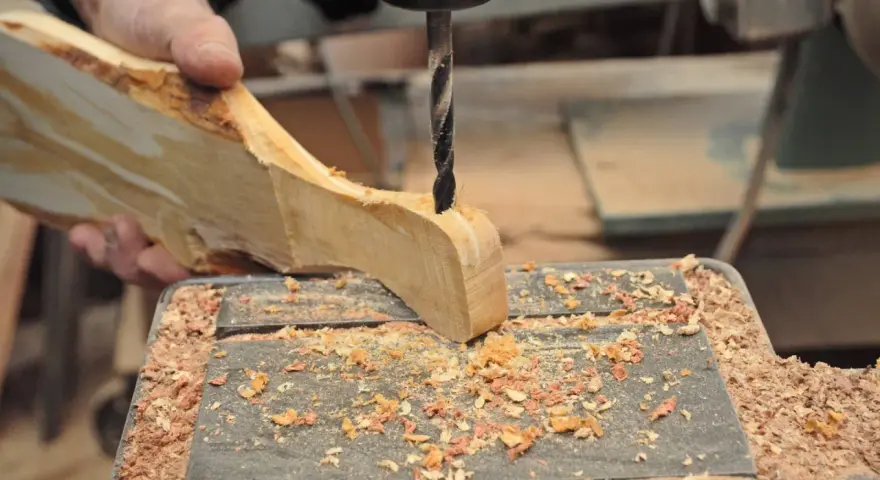 Mano che trapana un pezzo di legno grezzo, creando un tagliere legno fai da te. Segatura ovunque.