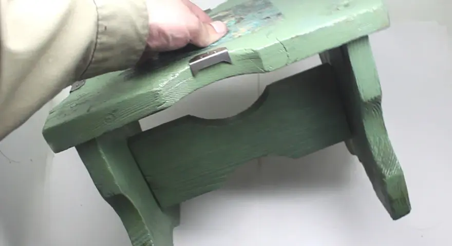 Mano che tiene uno sgabello di legno verde, pronto per verniciare con bomboletta spray.