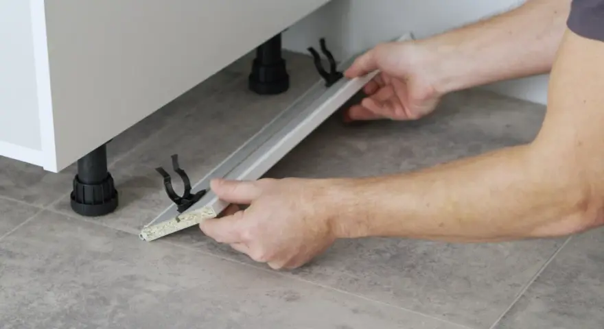 Mani che assemblano uno zoccolo cucina in alluminio, mostrando come tagliare e fissare i supporti.