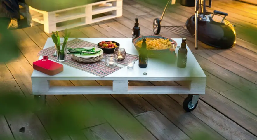 Tavolo con pallet fai da te, pronto per un barbecue con birre, patatine e pomodorini.