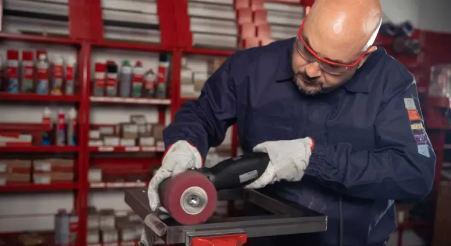 Operaio con occhiali protettivi e guanti lavora su un pezzo metallico, usando una smerigliatrice. Impara come saldare acciaio inox con precisione.