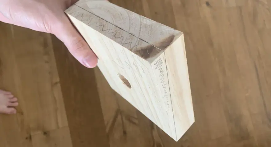 Mano che tiene un pezzo di legno con segni di matita, come se si stesse pensando a come tagliare il legno senza attrezzi.