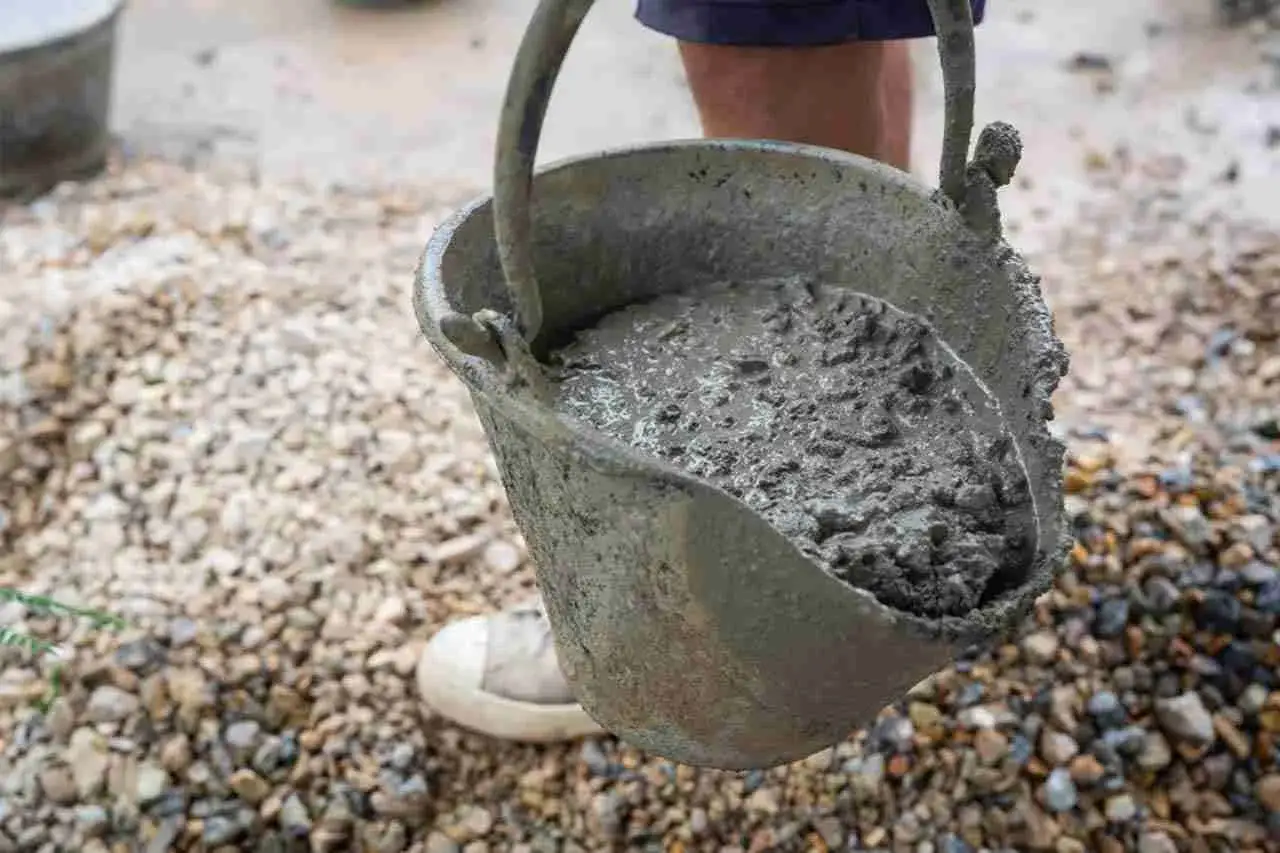 Secchio pieno di cemento fresco, pronto per essere utilizzato. Si vede come si fa il cemento, con ghiaia sullo sfondo.