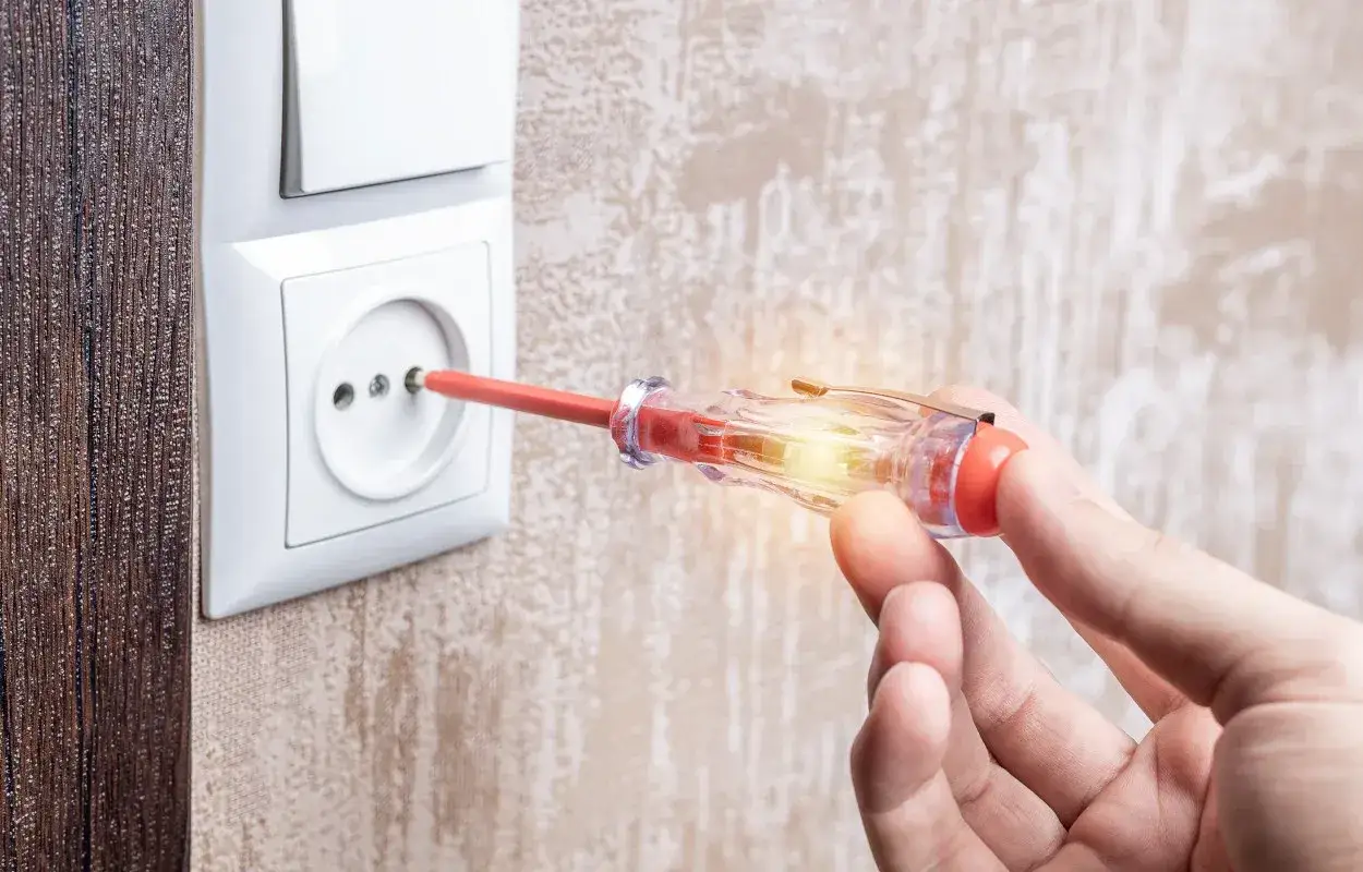 Mano che usa un cercafase per controllare una presa elettrica. La luce interna del cercafase si accende, indicando la presenza di corrente.