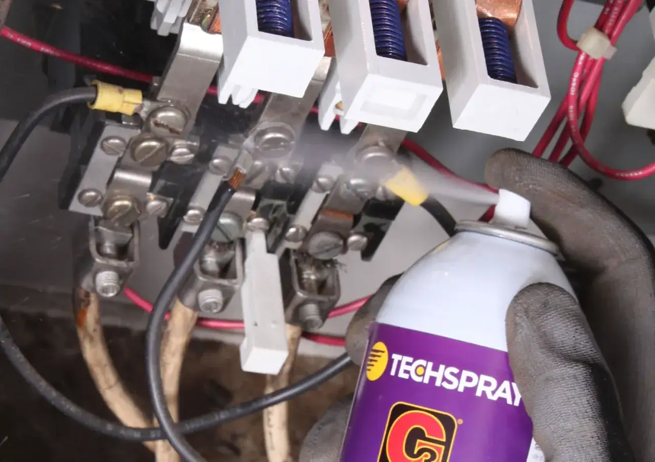 Mano guantata spruzza spray per come pulire contatti elettrici su morsetti metallici di un quadro elettrico.