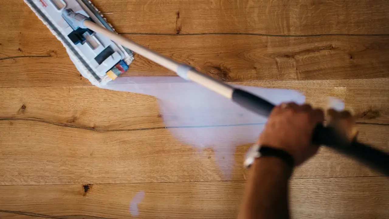 Mano che pulisce il parquet con uno straccio umido. Impara come decerare il parquet per un risultato impeccabile.