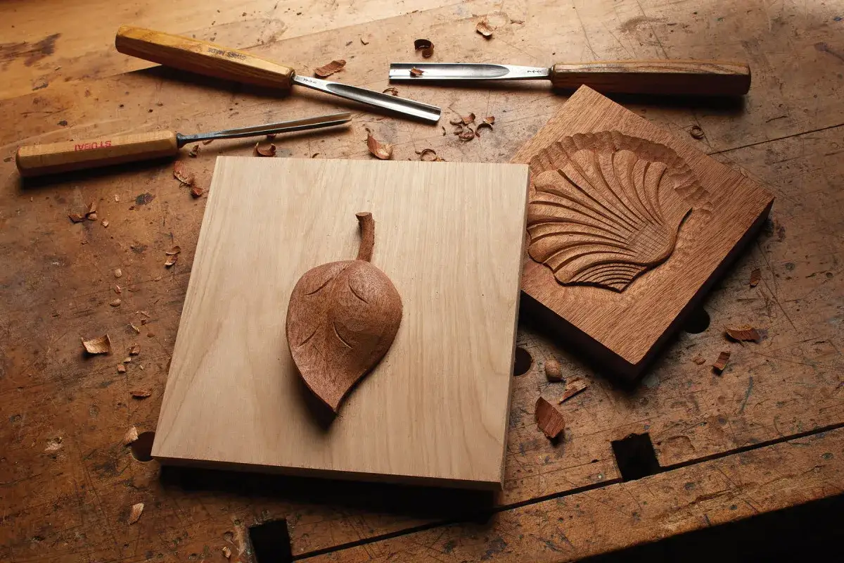 Attrezzi da intaglio e due sculture in legno: una foglia e una conchiglia. Un'ispirazione per chi vuole imparare come scavare il legno.
