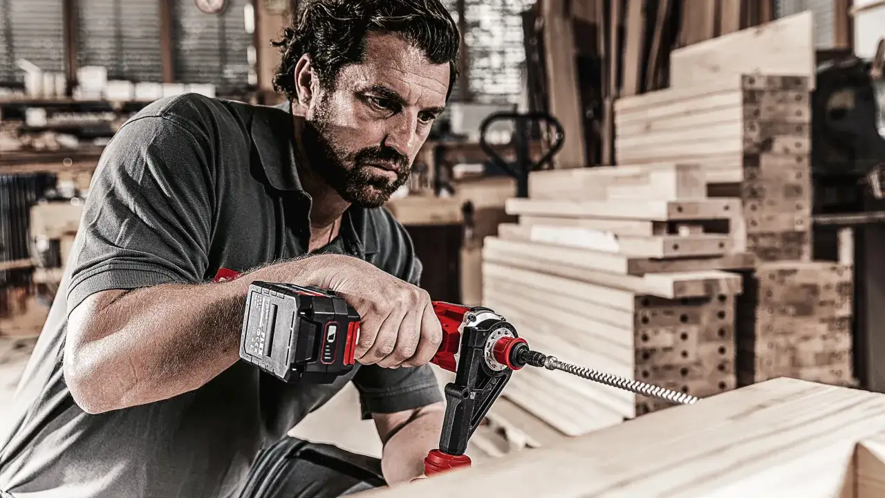 Falegname concentrato mentre mostra come si avvita un pezzo di legno con un trapano a batteria in officina.