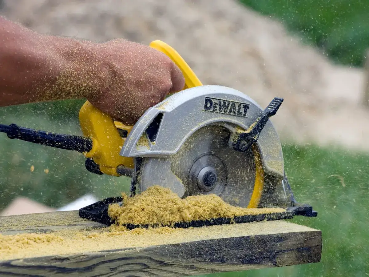 Mano che impugna una sega circolare DeWalt per tagliare legno, con segatura che vola ovunque.