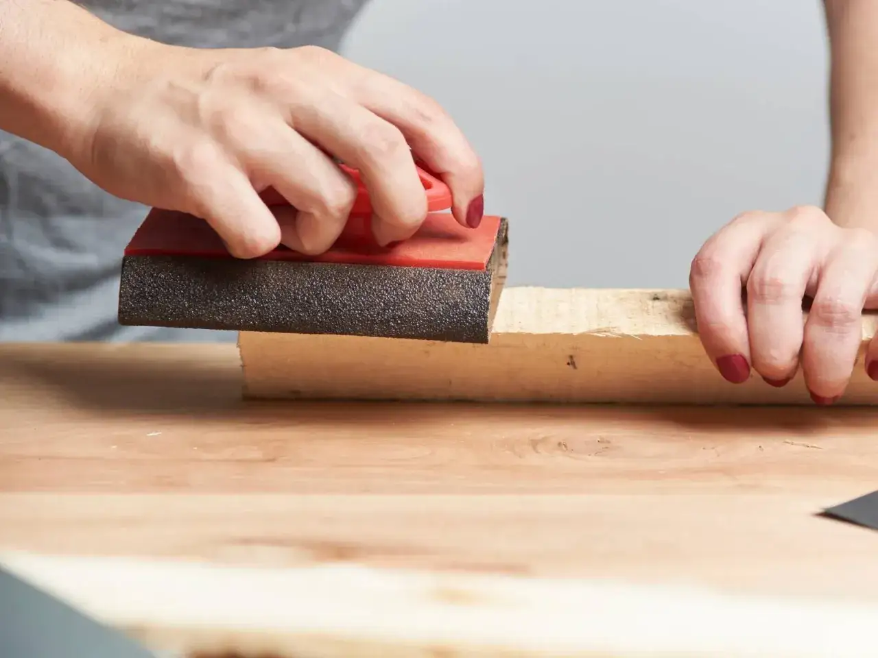 Mani che levigano un pezzo di legno con carta vetrata per rimuovere la colla.