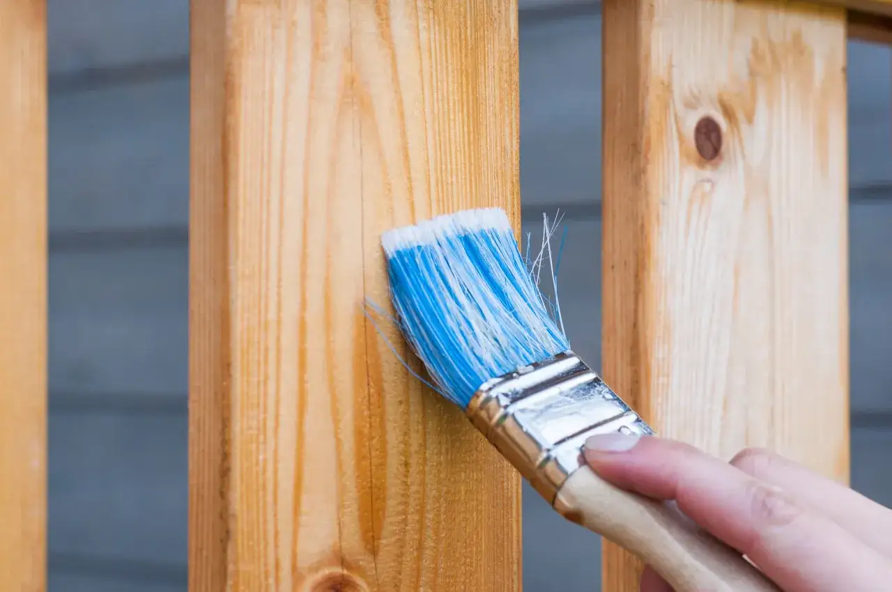 Mano che applica una tinta per scurire il legno su una staccionata di pino.