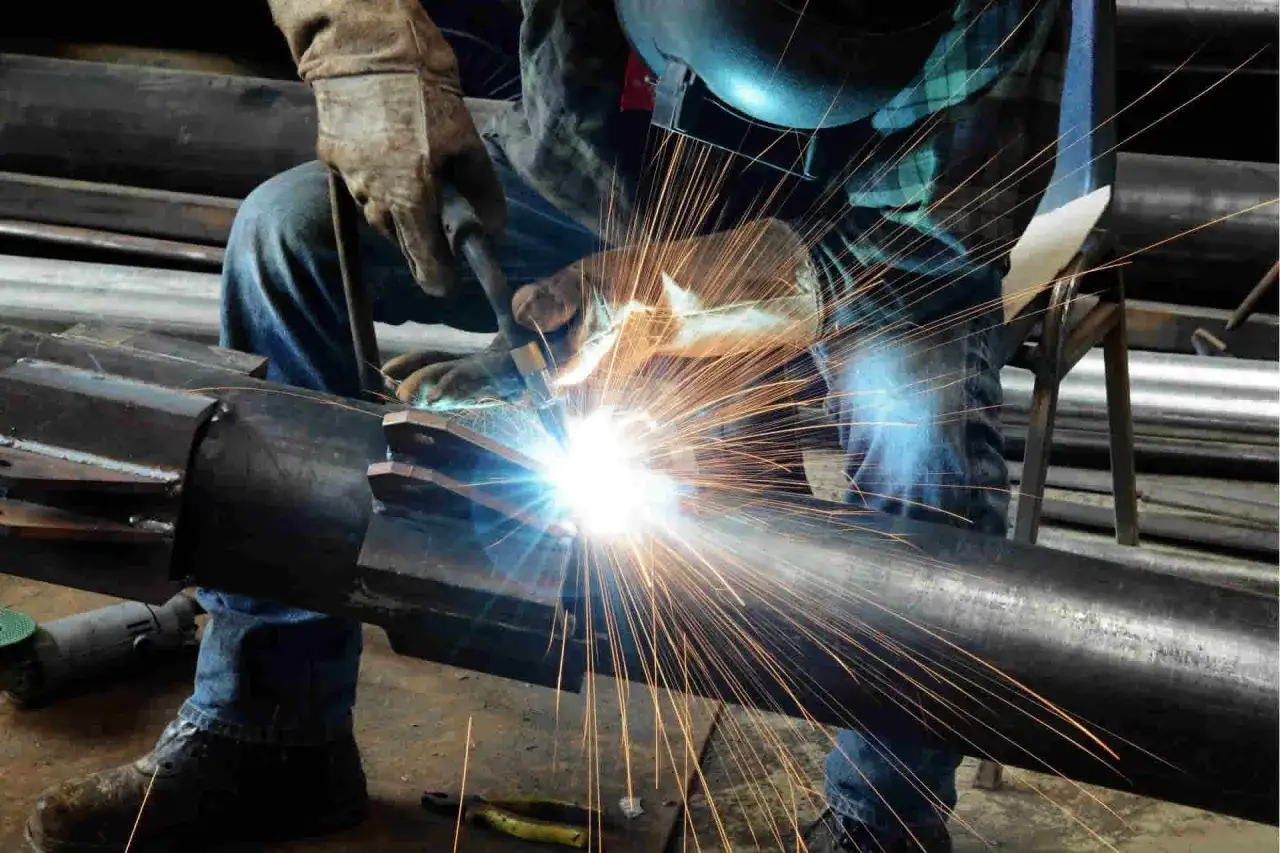 Saldatore al lavoro, con scintille che volano mentre usa uno dei tanti tipi di elettrodi per saldatura su un grosso pezzo di metallo.