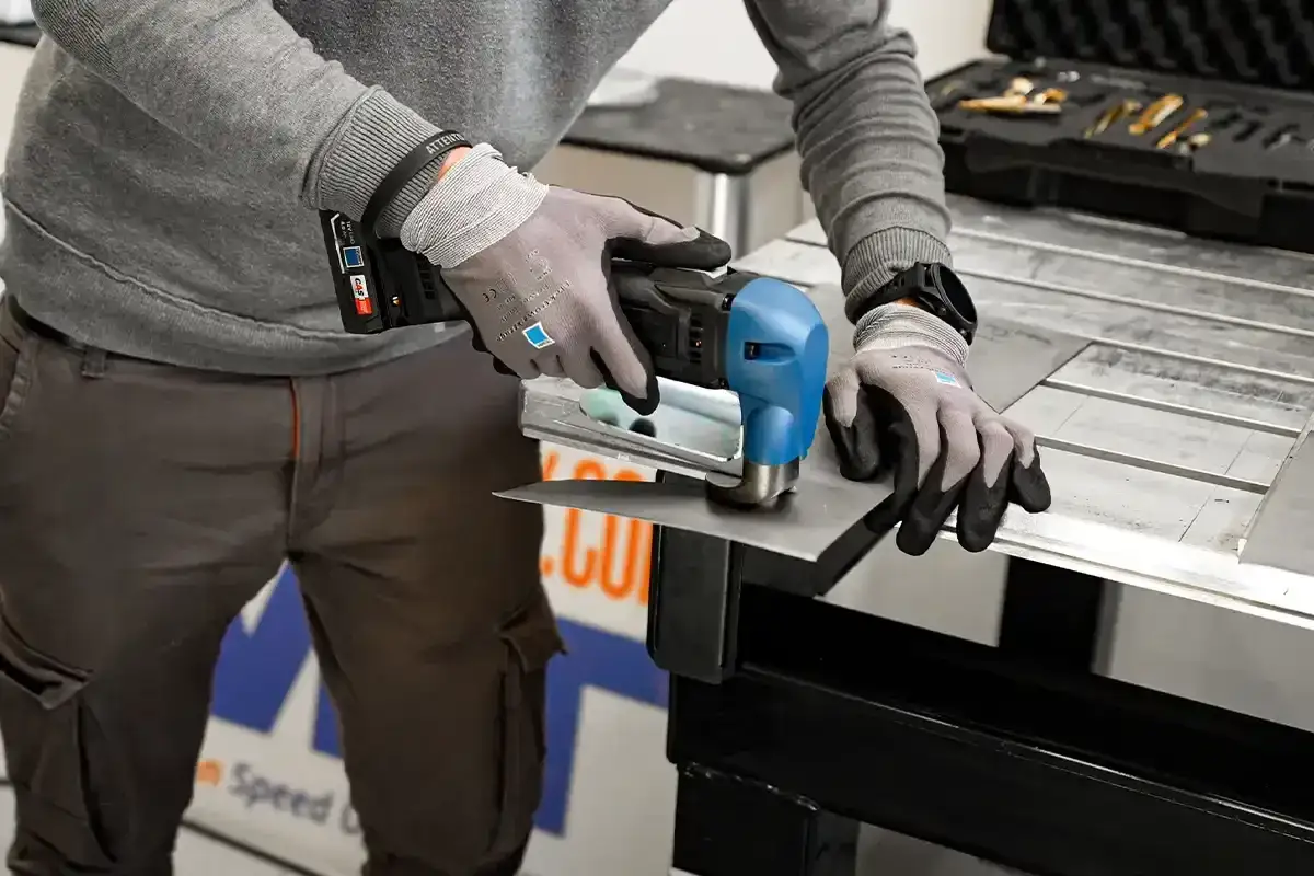 Uomo con guanti usa un utensile elettrico per tagliare lamiera. L'utensile non parte se la batteria è scarica.