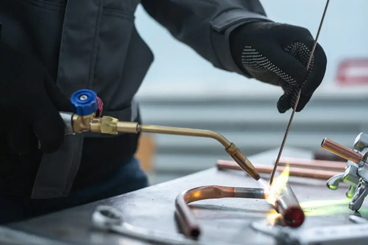 Un tecnico esegue una saldobrasatura ferro su tubi di rame, usando una torcia per fondere il metallo d'apporto.
