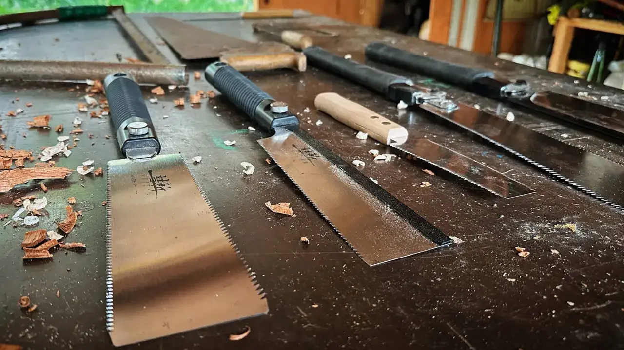 Vari tipi di seghe, con lame sottili e denti affilati, pronte per il lavoro sul banco da falegname, tra trucioli di legno.