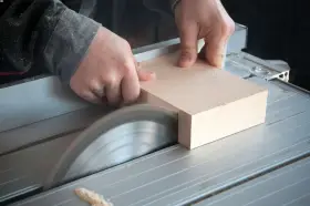 Mani esperte guidano un pezzo di legno su una sega circolare per tagliare legno a mano con precisione.