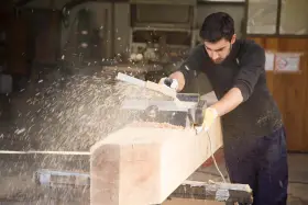 Falegname usa pialla elettrica su un grosso tronco di legno, creando una nuvola di segatura. Il piallare significato è dare una finitura liscia.
