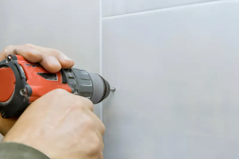 Mani che usano un trapano per fare un buco nel muro bianco.