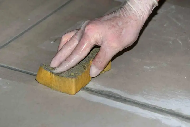 Mano con guanto in lattice che rifinisce le fughe dei pavimenti con una spugna umida.