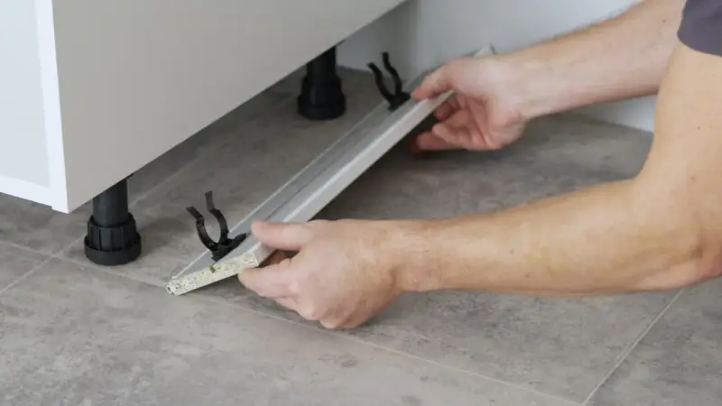 Mani che assemblano uno zoccolo cucina in alluminio, mostrando come tagliare e fissare i supporti.